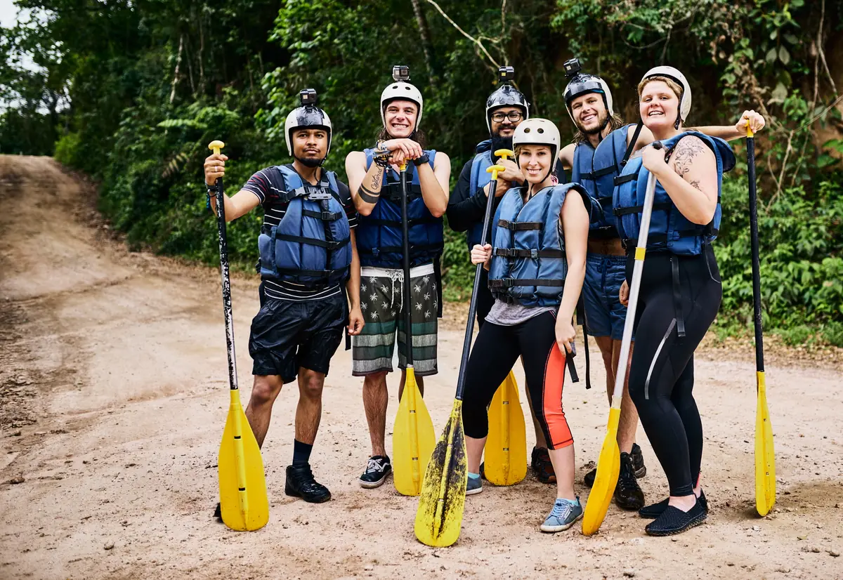 A group geared up with helmets, life jackets and paddles