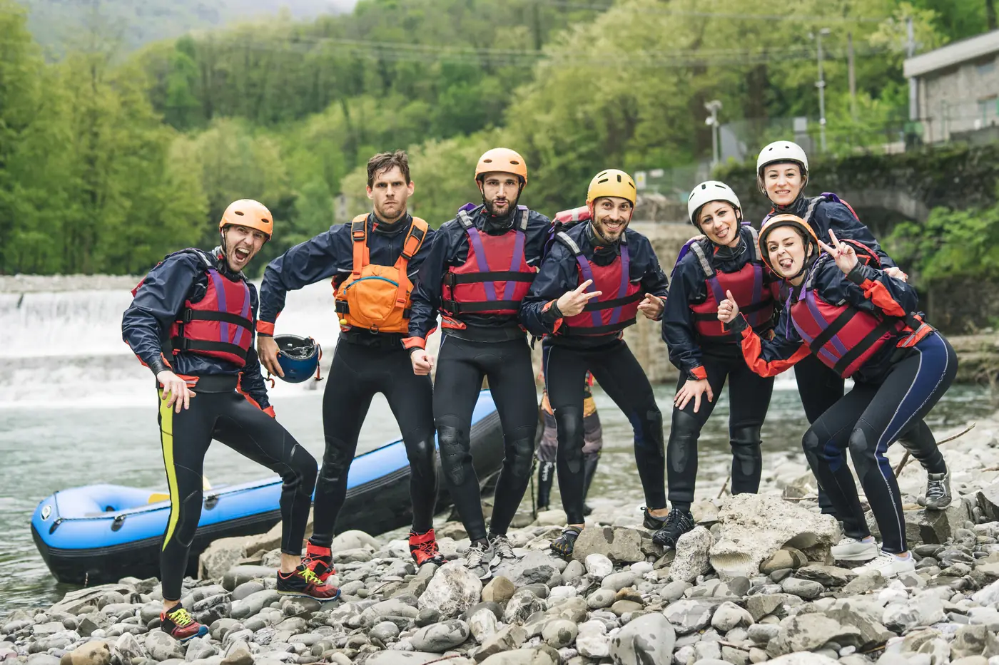 A rafting group in wetsuits and helmets posing beside the river